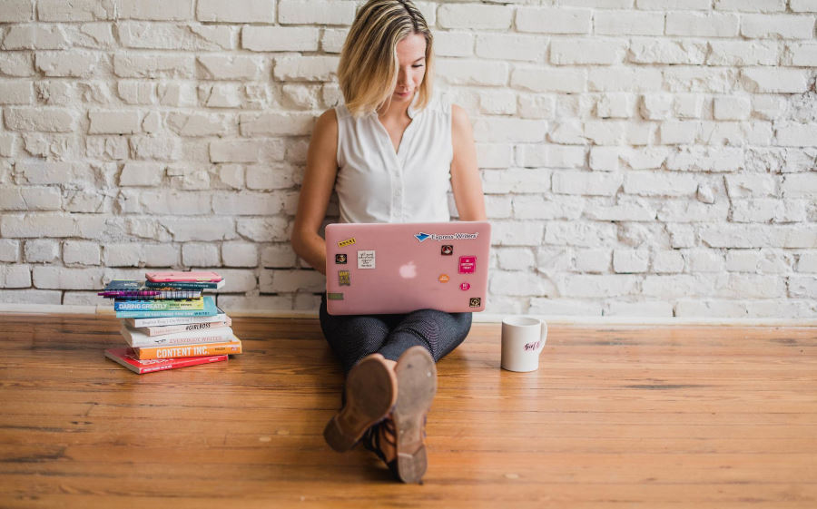 Woman sitting on ground working on pink laptop